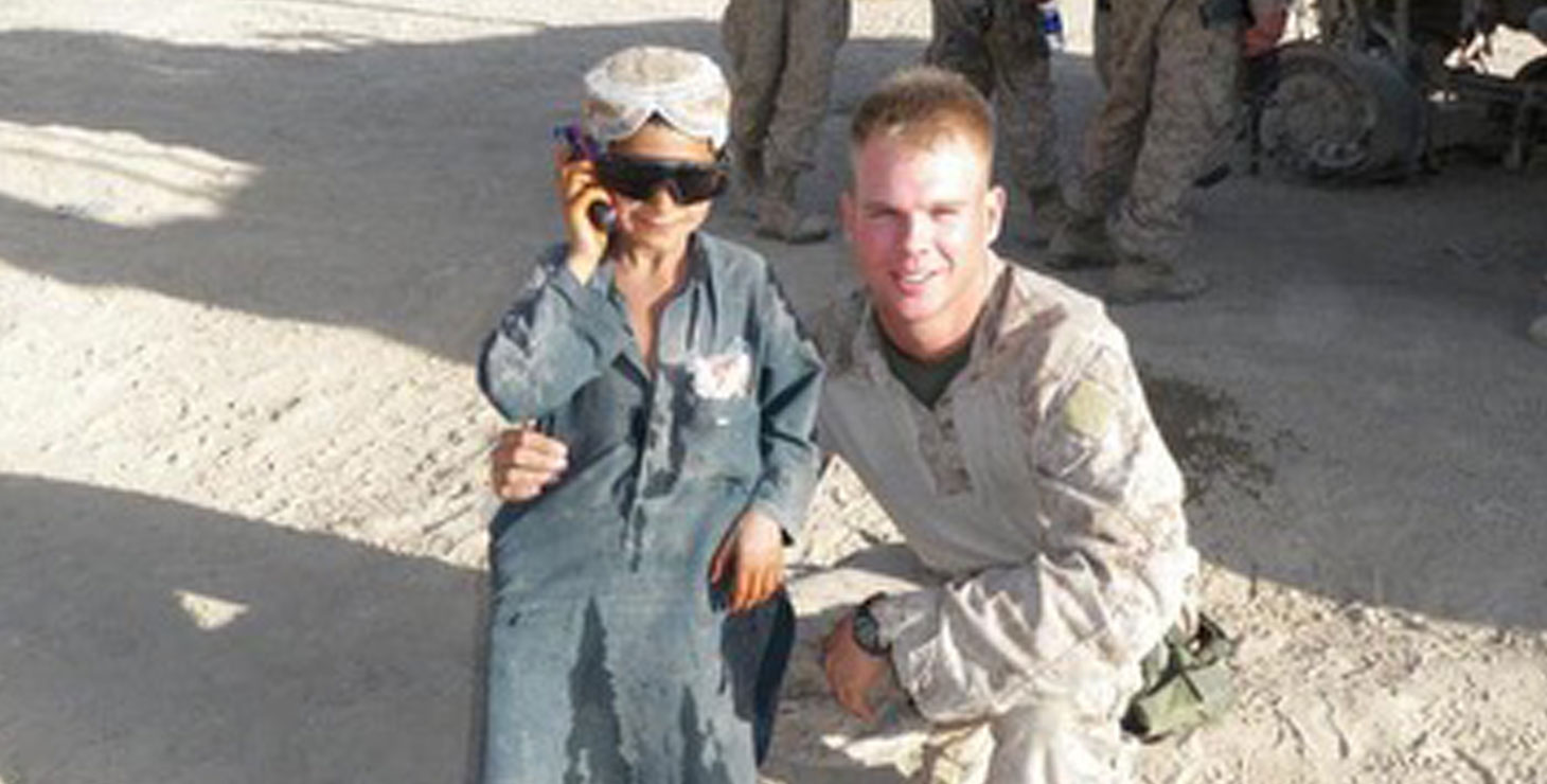 A photo of Captain Kyle Gettings in uniform posing with a kid in sunglasses.